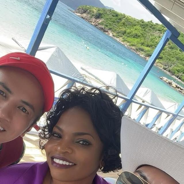 Mechiel with two guests on a covered deck above a turquoise bay lined with white beach umbrellas