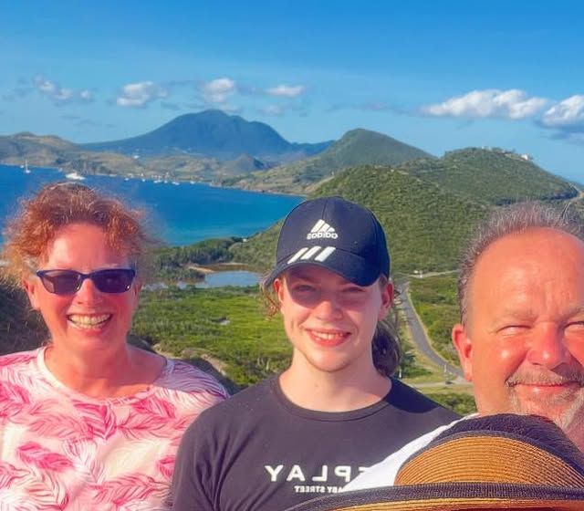 Three guests taking a selfie at a lookout on St. Kitts, with the Southeast Peninsula and Nevis Peak behind them