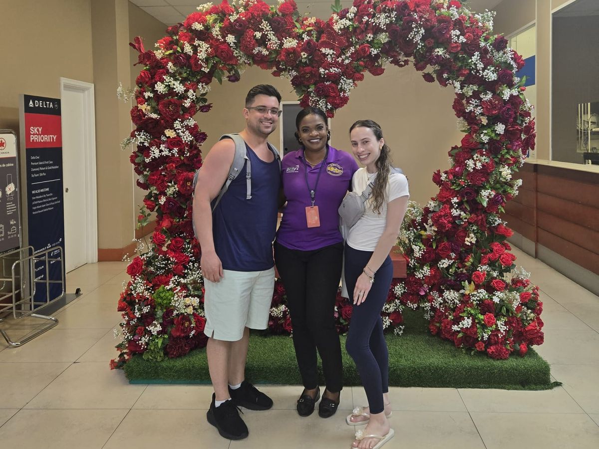 Mechiel standing with two guests in the arrivals hall at SKB airport, in front of a heart-shaped arch of red and white flowers