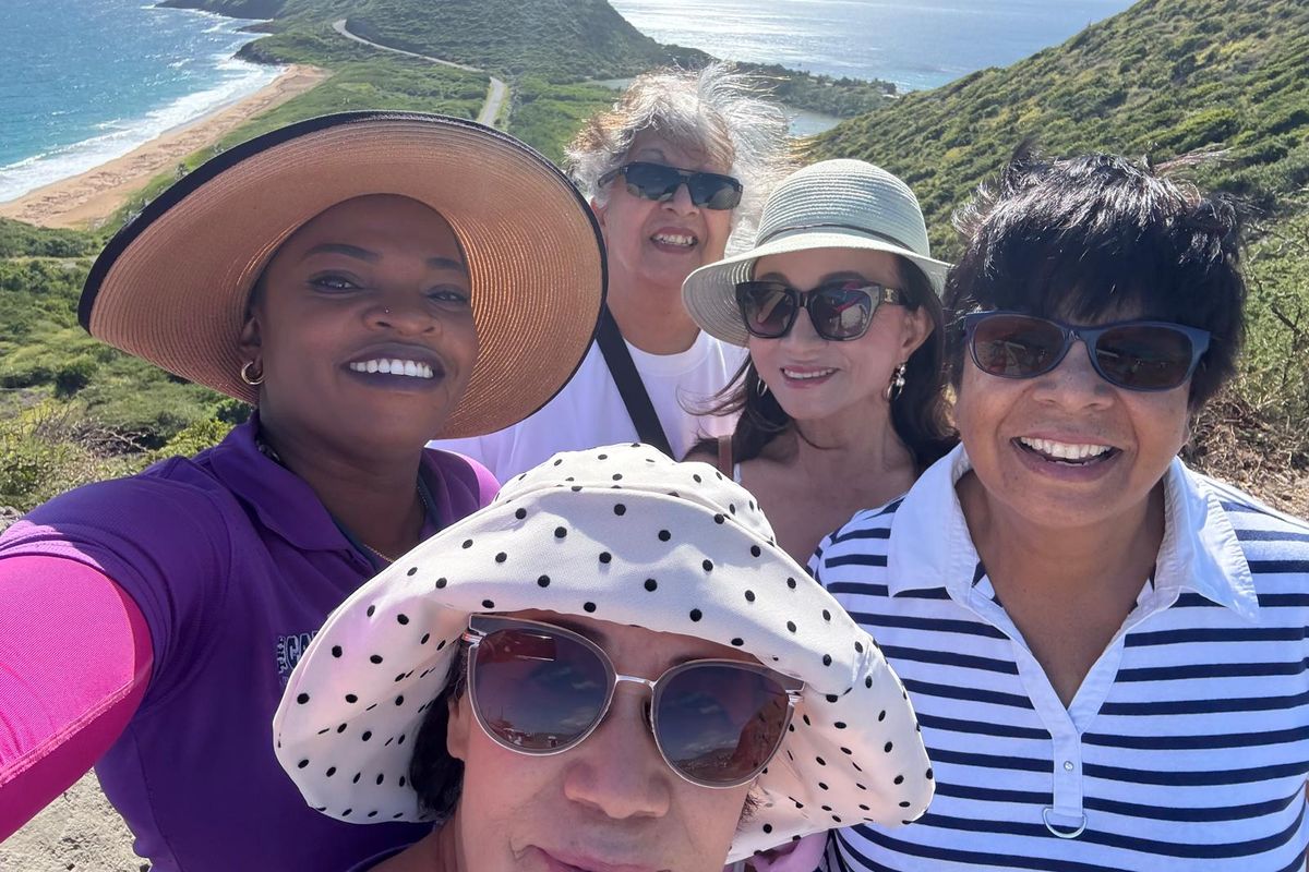 Selfie of Mechiel in a sun hat with four smiling guests at the Timothy Hill lookout, with a sandy bay, the peninsula road and green hills behind them